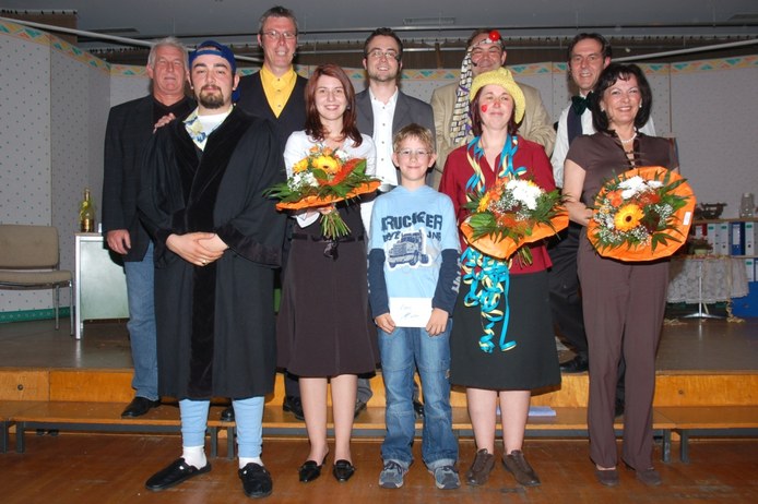 Die Theatergruppe nach der Aufführung vor der Bühnenkulisse, mehrere Darsteller noch im Kostüm, drei mit großen Blumensträußen
