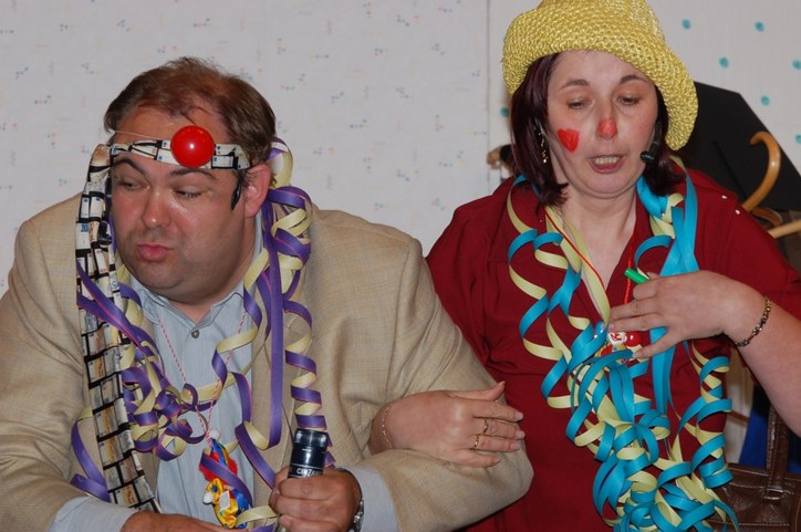 Szene aus dem Schwank: ein Darsteller mit roter Clownsnase und Luftschlangen um den Hals, daneben eine Darstellerin mit Strohhut und aufgemaltem Herz auf der Wange