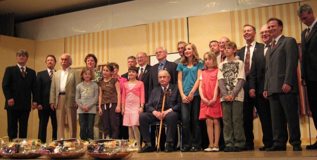 Die geehrten Mitglieder, Erwachsene und Kinder, gemeinsam auf der Bühne des Bürgerhauses, davor Geschenkkörbe