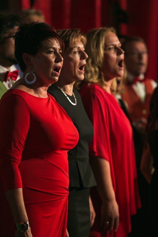 Drei Sängerinnen in roten und schwarzen Kleidern singen nebeneinander, in warmes rotes Bühnenlicht getaucht