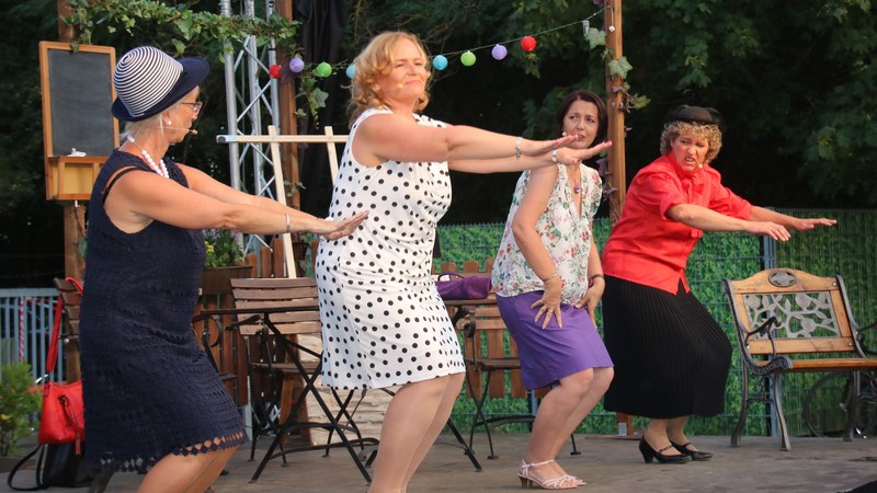 Vier Darstellerinnen in sommerlichen Kleidern bei einer schwungvollen Tanzeinlage auf der Freilichtbühne