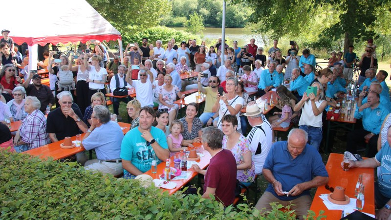 Dicht besetzte Biertischgarnituren beim Sommerfest am Vereinsheim, viele Gäste fotografieren mit dem Handy, im Hintergrund der Main