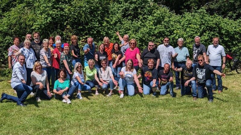 Der Chor Crescendo auf einer Wiese, viele Sängerinnen und Sänger in Queen-T-Shirts, winkend in die Kamera