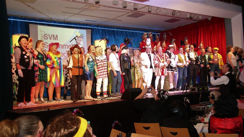 Alle Mitwirkenden singen kostümiert das Finale auf der Bühne, im Vordergrund das Publikum im Saal