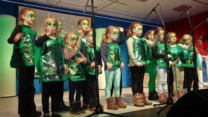 Der SVM-Kinderchor als Drachenkinder in grün glänzenden Umhängen mit geschminkten Gesichtern auf der Bühne