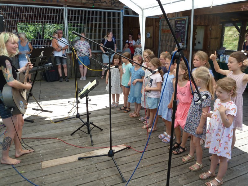 Eine Chorleiterin mit Gitarre begleitet die singenden Kinder beim Kindernachmittag am Vereinsheim