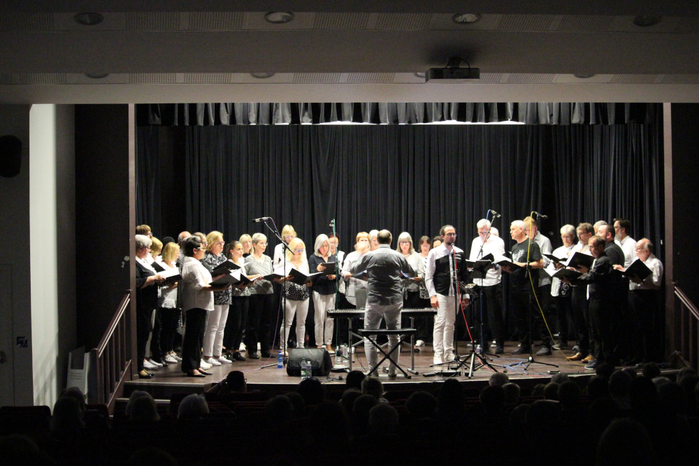 Der Chor Crescendo singt beim Gemeinschaftskonzert auf einer Bühne, davor der dirigierende Chorleiter