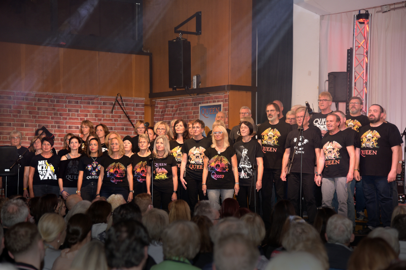 Der singende Chor Crescendo in Queen-T-Shirts, im Vordergrund die Köpfe der Zuschauer